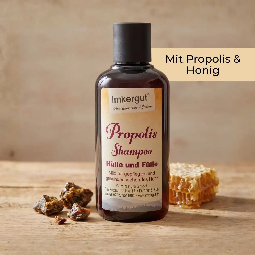 Eine Flasche Propolis Shampoo steht auf einem Holztisch neben Propolisstücken und einer Honigwabe, im Bild steht der Text „Mit Propolis & Honig“