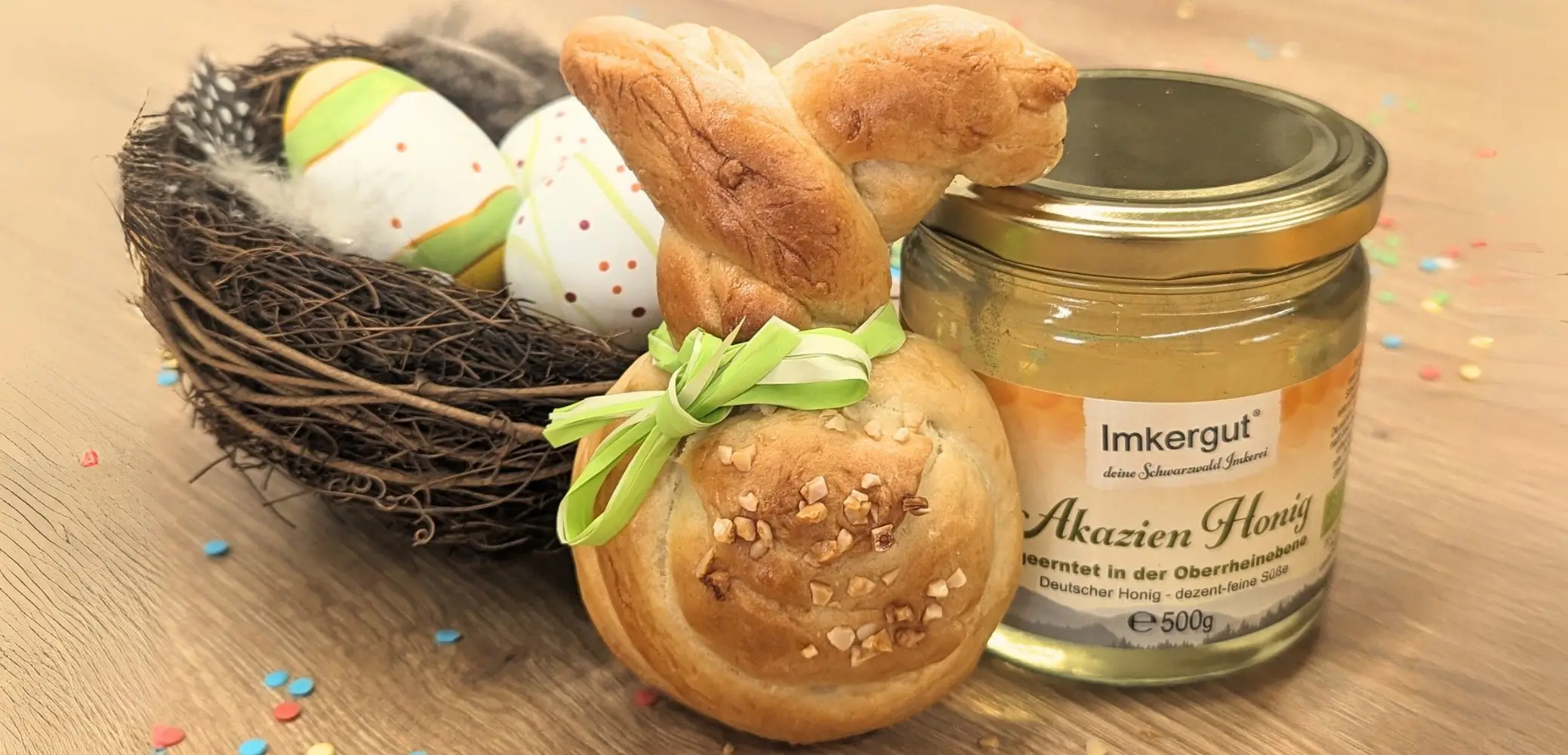 Hefeteig-Osterhase mit grünem Band um den Hals, daneben ein Glas Akazienhonig
