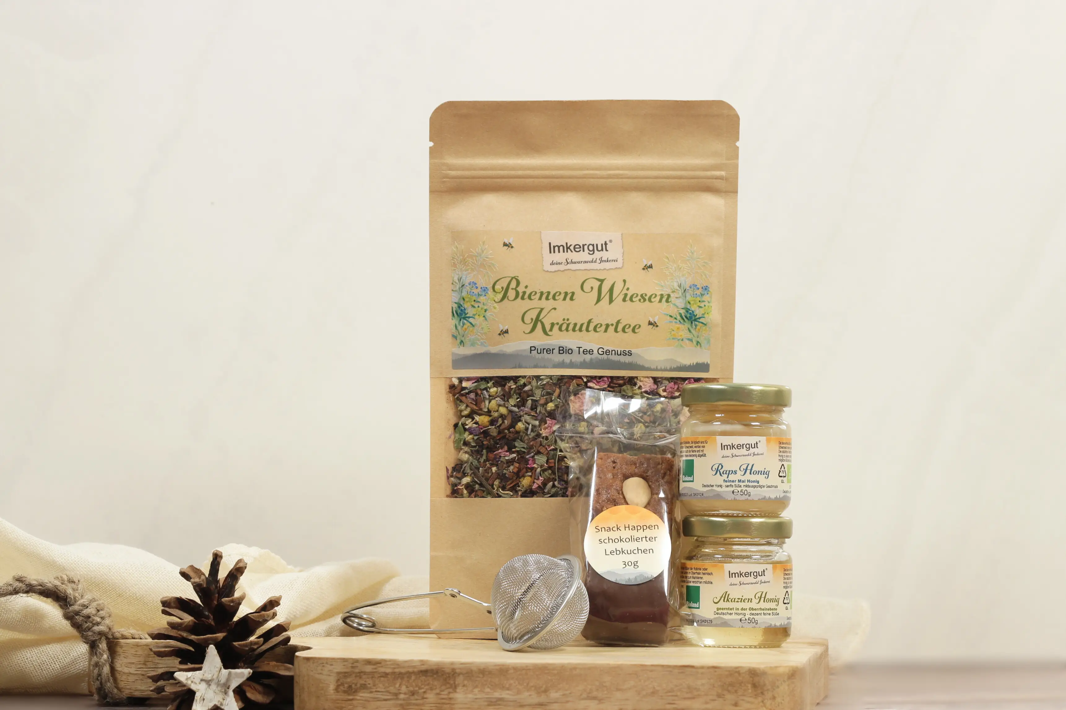 Eine Packung Tee, zwei kleine Gläesr Honig, ein Teesieb und ein Lebkuchen auf einem Holzbrett