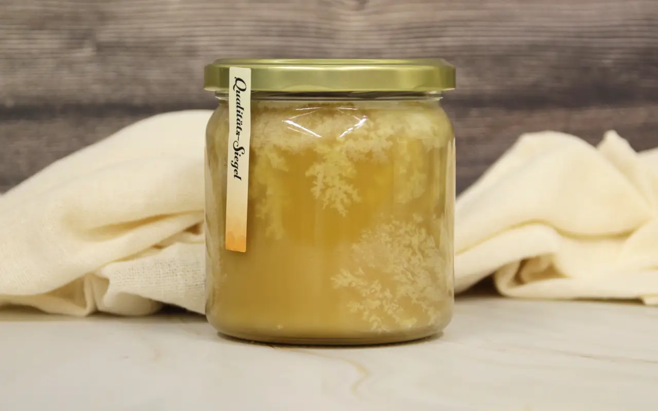 Ein Glas Sommerblütenhonig mit sichtbaren Zuckerkristallen