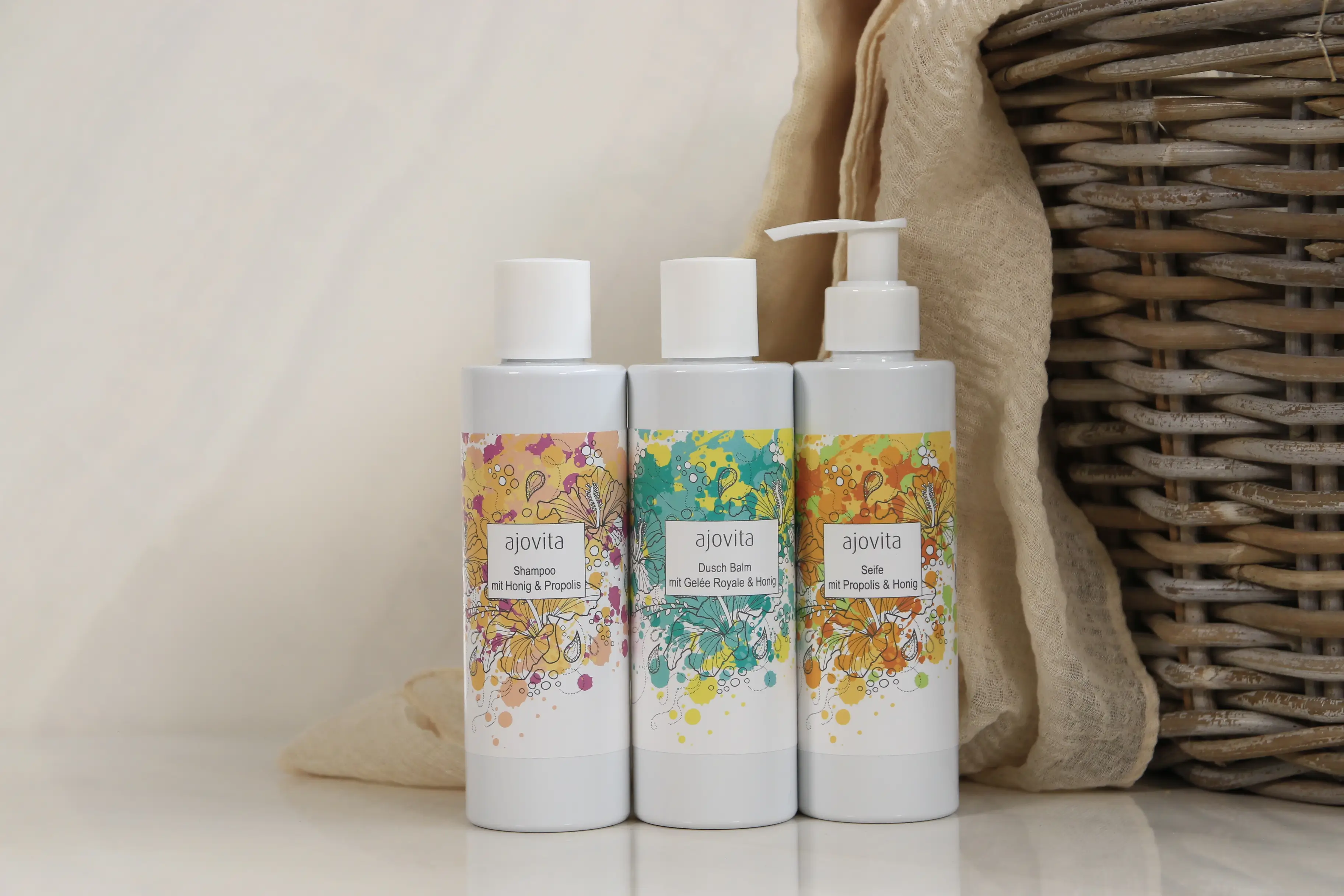 Die drei ajovita-Produkte Seife, Duschgel und Seife nebeneinander, im Hintergrund ein Tuch und ein Korb