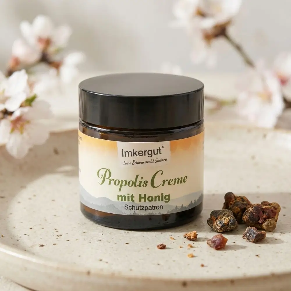 Propolis Creme steht auf einem beigen Tablett mit Rohpropolis. Im Hintergrund sind weiße Kirschzeige