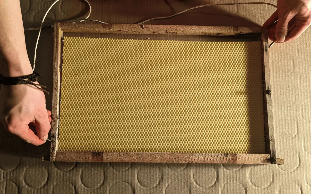 Eine Hand, die eine Wachsplatte in ein Rähmchen einlötet