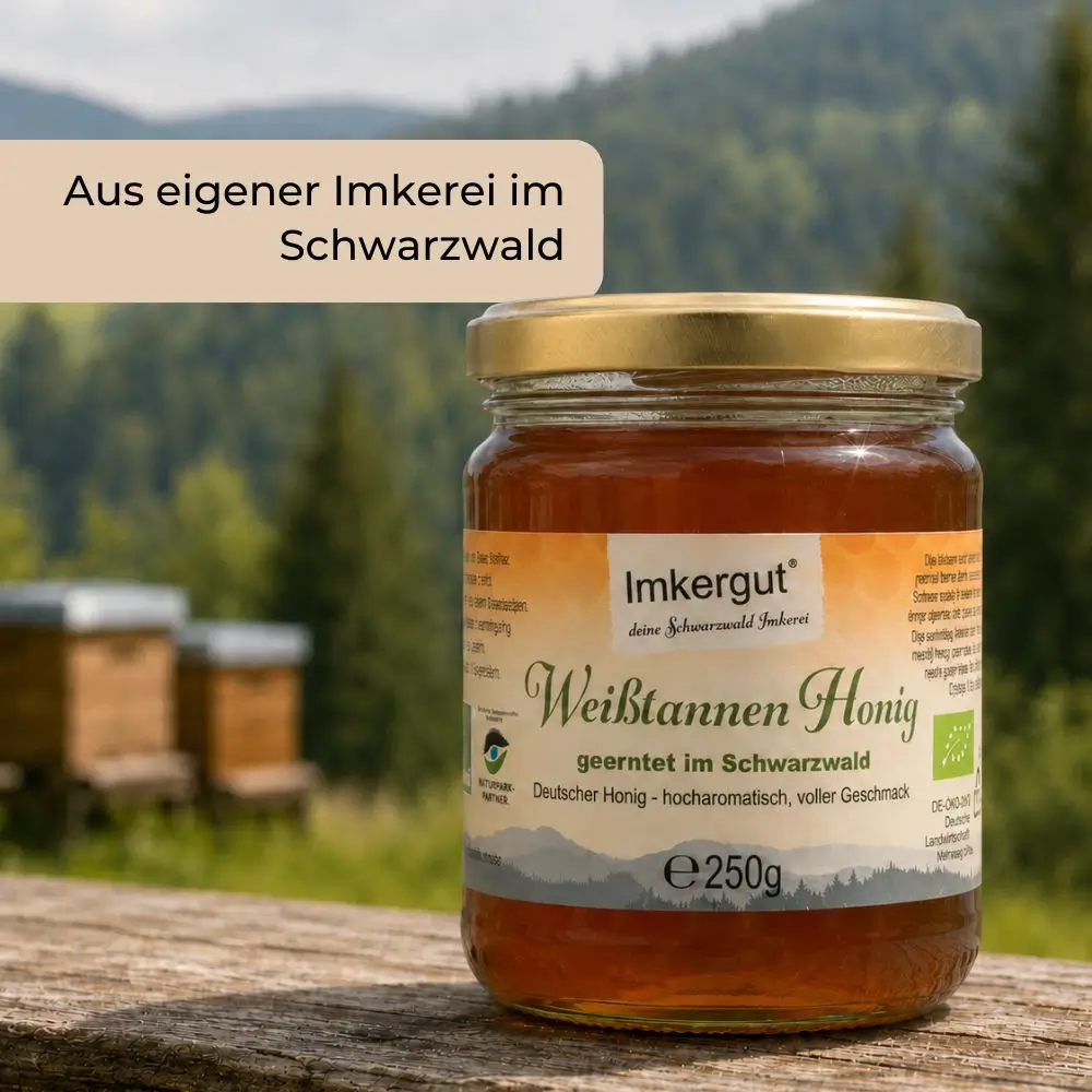 Glas Weißtannenhonig steht auf einem Holzbalken im Schwarzwald.  Im Hintergrund sieht man zwei Bienenstöcke. Im Bild ist ein Textfeld: Aus eigener Imkerei im Schwarzwald